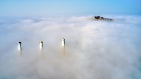 Three chimneys and a mountain rise out of the clouds.