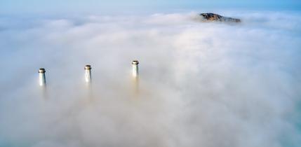 Three chimneys and a mountain rise out of the clouds.
